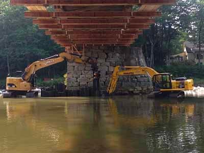 Excavators rebuilding stone pier under Blair bridge over river