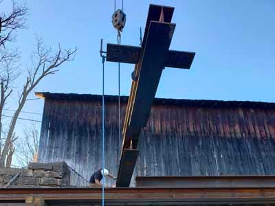 Grange City covered bridge with large black cross being lifted by crane over stone abutment