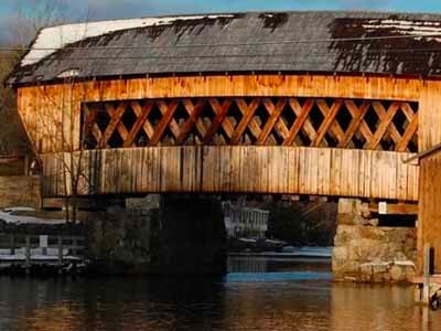 Squam River covered bridge exterior close-up showing lattice truss pattern over river in winter