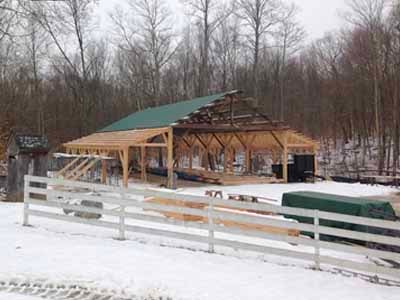 Perry barn timber frame with green metal roof and white fence in winter