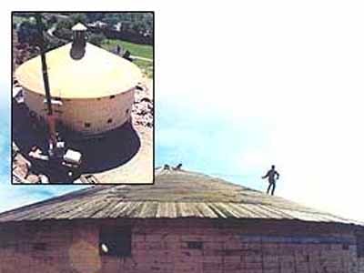Worker standing on round barn roof with aerial inset showing cupola installation
